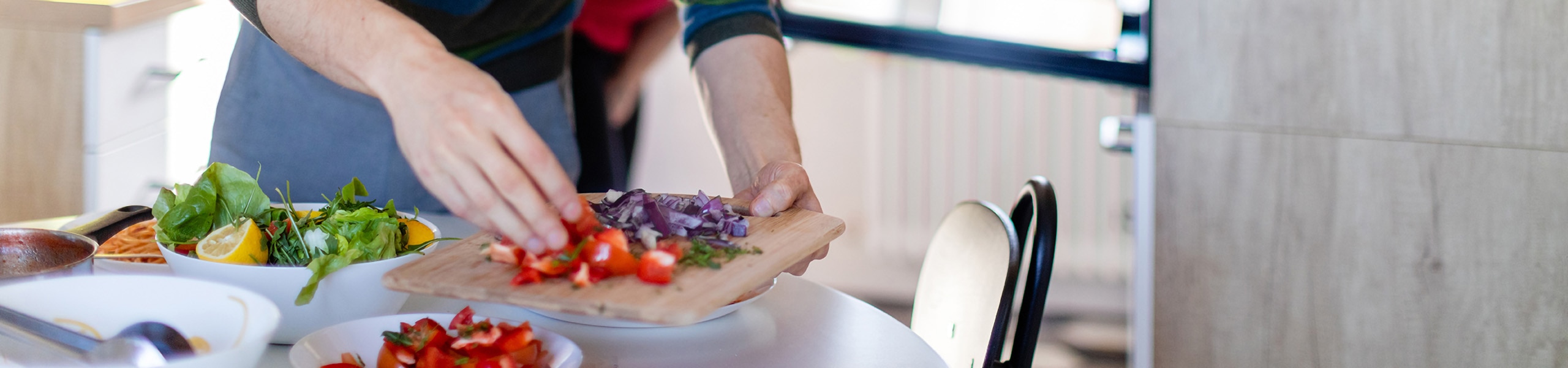 Persona en la cocina colocando hierbas y vegetales en una tabla de cortar