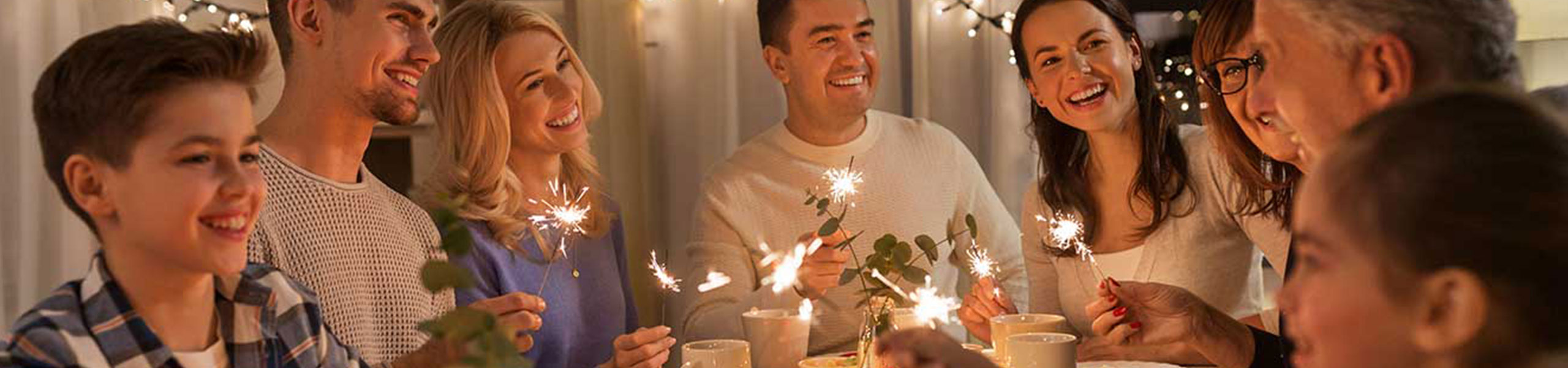 Una familia sonriente reunida alrededor de la mesa sosteniendo luces de bengala