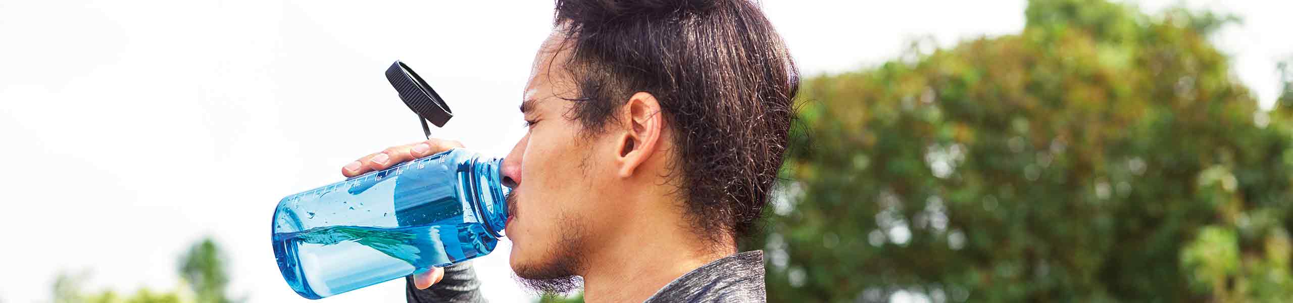 Man in exercise clothing drinks water outdoors.