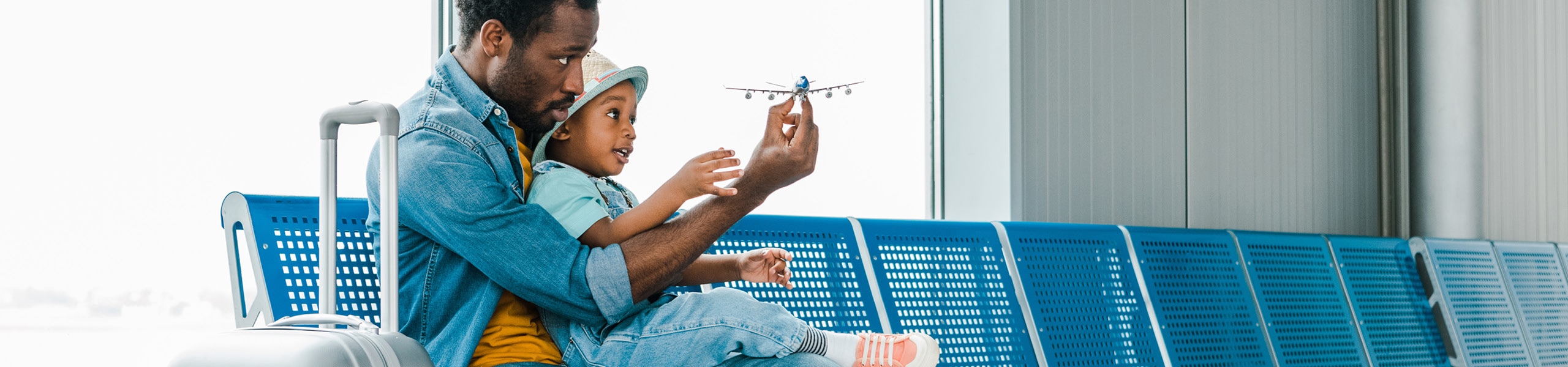 Padre sosteniendo a su hijo pequeño y mostrándole un avión de juguete en el aeropuerto 