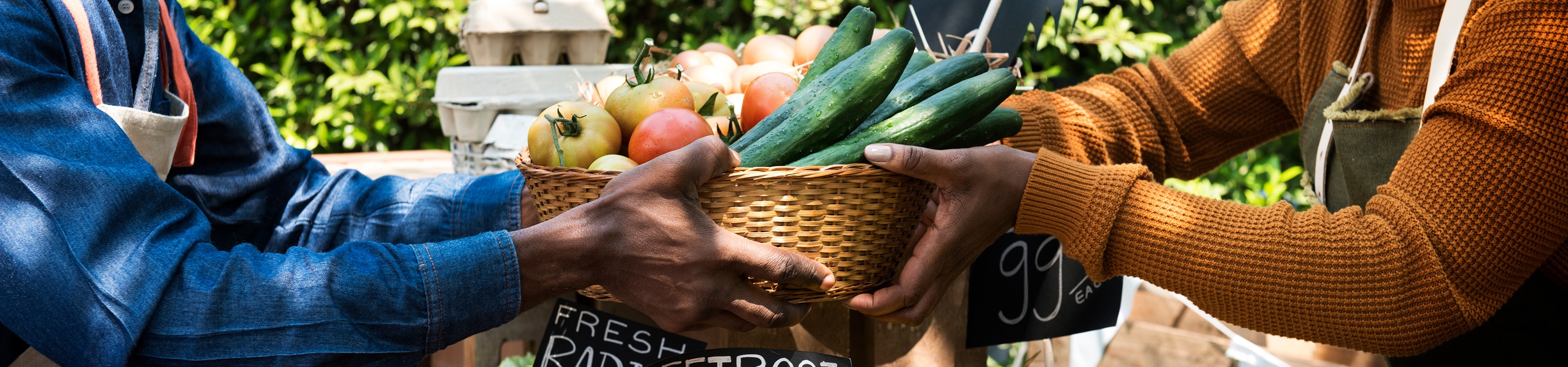 Una persona ofreciendo a alguien una canasta de verduras en un mercado al aire libre 