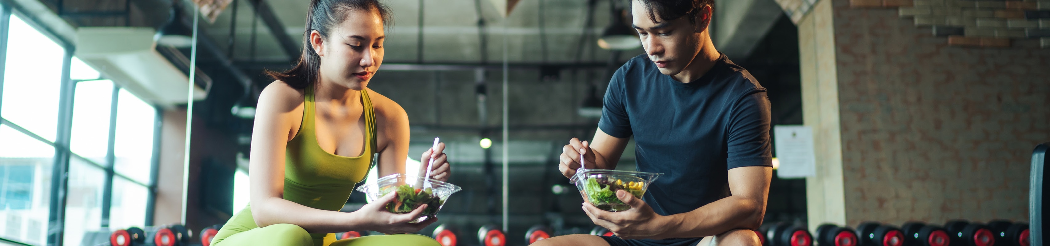 Dos deportistas comiendo ensaladas pequeñas en el gimnasio