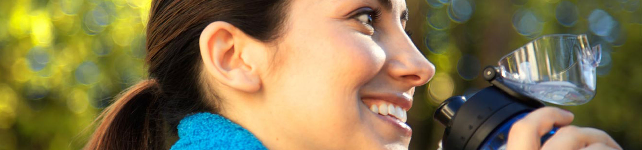 Una mujer sonriente bebe agua al aire libre.