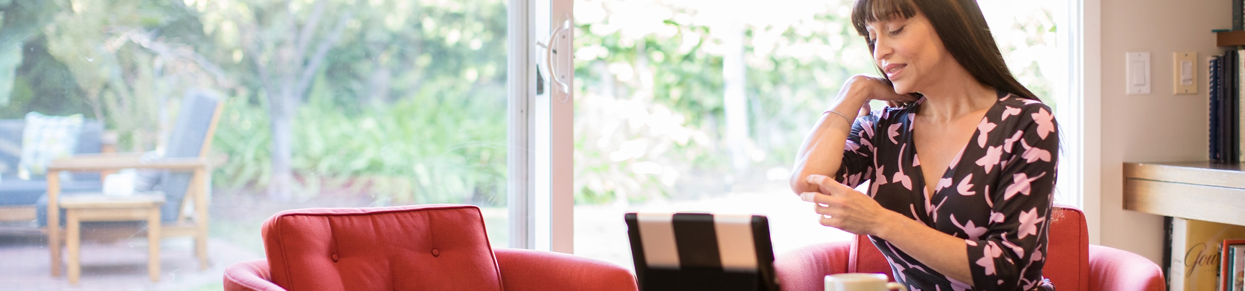 Mujer sentada en casa frente a su computadora portátil, señalándose el codo.