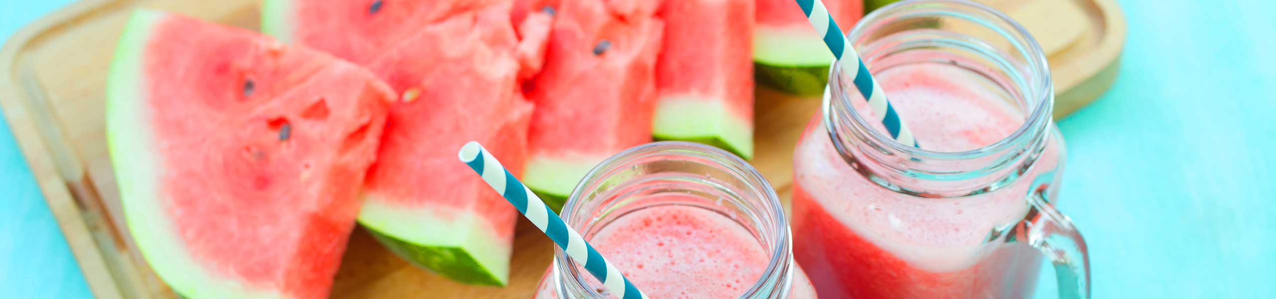 slices of watermelon next to cups of watermelon juice.