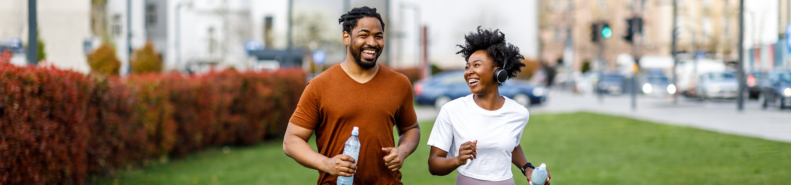 Una pareja sonriente con ropa deportiva trotando por un parque en la ciudad. 