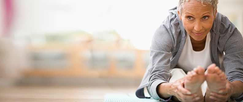 Mujer que se estira hacia adelante en un mat para yoga