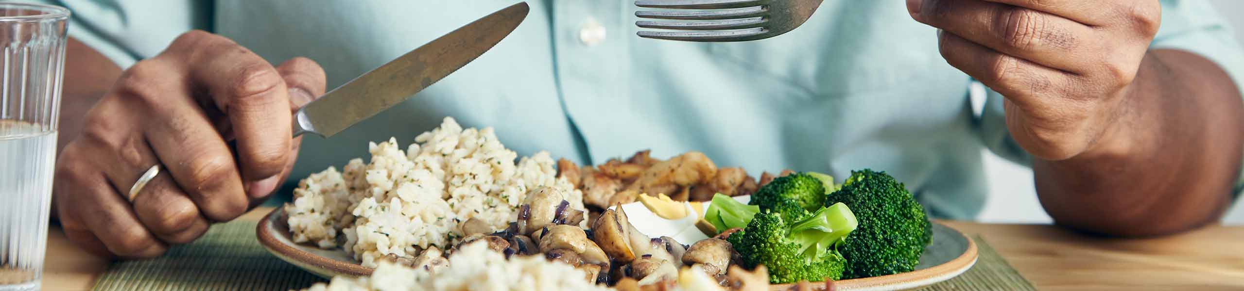 A man eating a healthy protein lunch, made of chicken, rice, and broccoli 