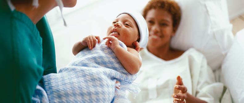 Médica acercando un bebé recién nacido a la madre.