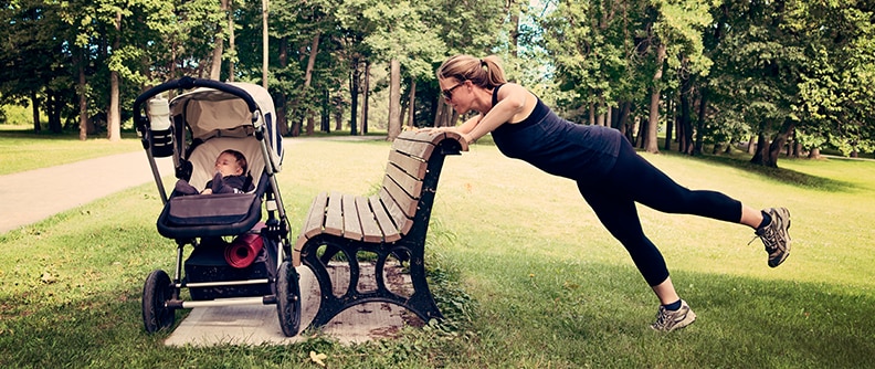 Madre haciendo ejercicio en un parque junto al bebé en el cochecito.