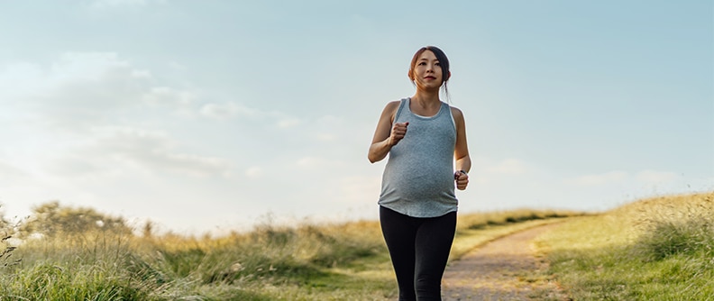 Mujer embarazada corriendo en el parque bajo un cielo azul claro.