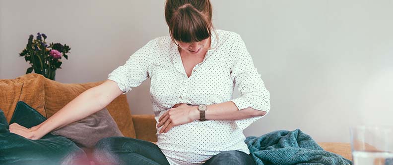 Mujer embarazada (9 meses de gestación) sentada en el sofá de su hogar tomando el tiempo entre una contracción y la otra.