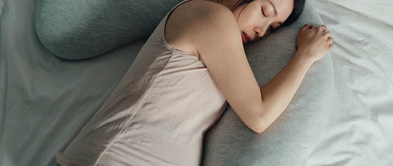 Mujer embarazada durmiendo en la cama con almohadones.