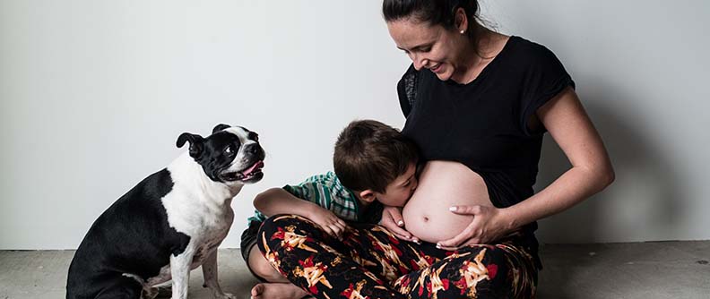 Madre e hijo sentados en el piso. Hijo besando el vientre de su mamá.