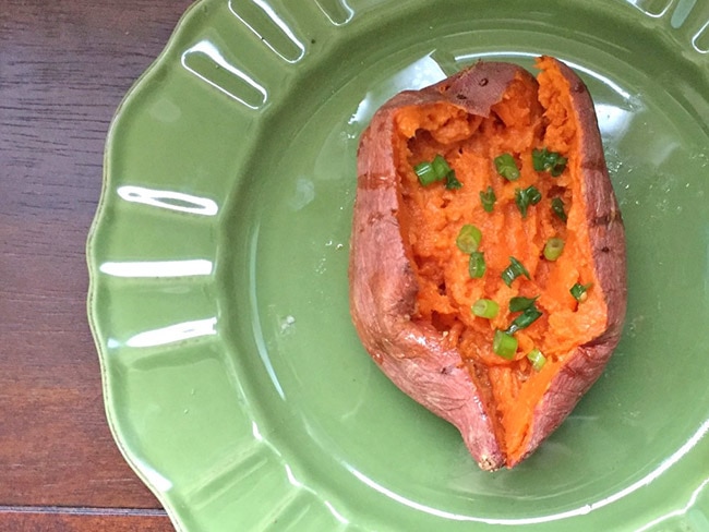 Baked sweet potato with chopped scallions on a green plate on a wooden table.