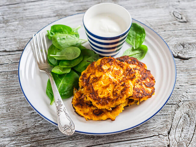 Yam pancakes, spinach, and yogurt on a white plate on a wooden table. 