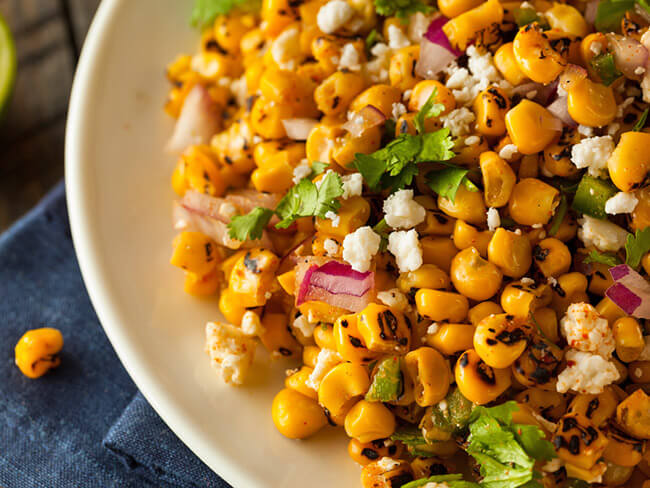 Esquites or roasted corn kernels with Cotija cheese on a plate.