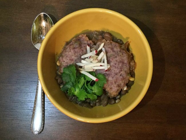 Bowl of bean stew with dumplings topped with cilantro and julienned radishes