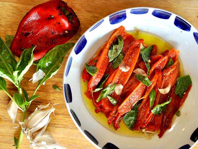 Roasted red peppers in virgin olive oil and garnished with torn basil leaves and shaved garlic.
