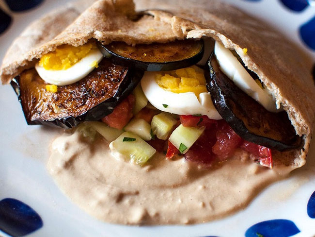Whole-wheat pita pocket stuffed with seared eggplant, hard-boiled eggs, tomatoes, cucumbers, and tahini spread