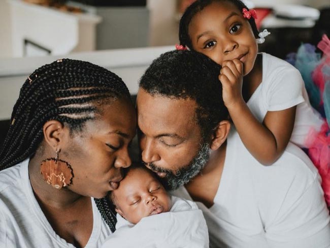 Mother and father kissing newborn baby’s head.