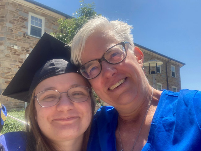 A middle-aged woman smiling with her daughter at her daughter's college graduation.