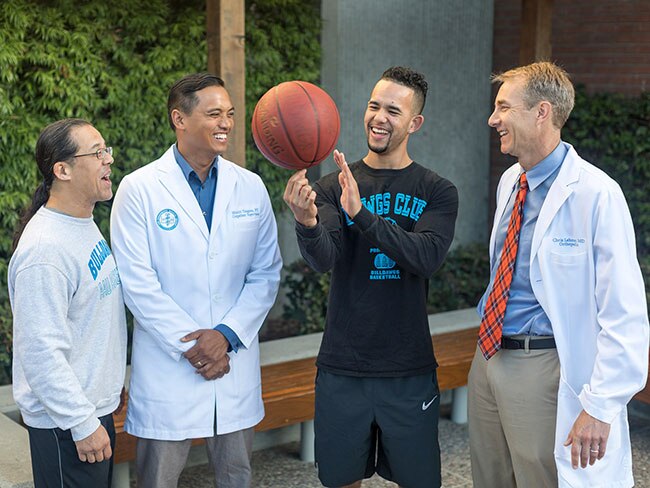 Young man and his father with basketball, surrounded by a group of doctors in lab coats.