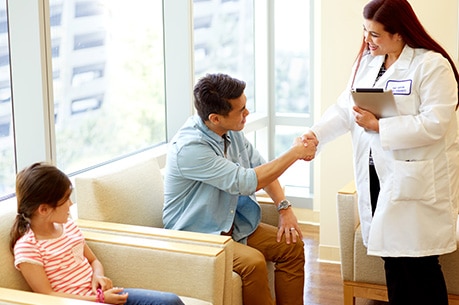 Enfermera hablando con un padre y su hija en un consultorio médico