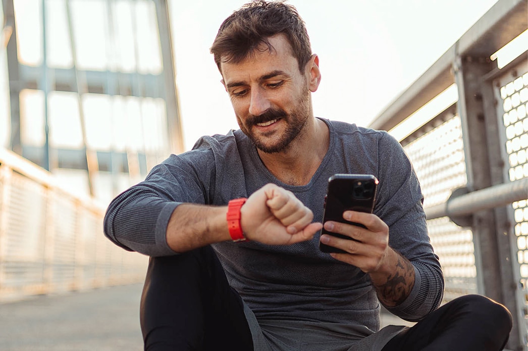 Persona revisando un dispositivo portátil mientras sostiene un teléfono móvil