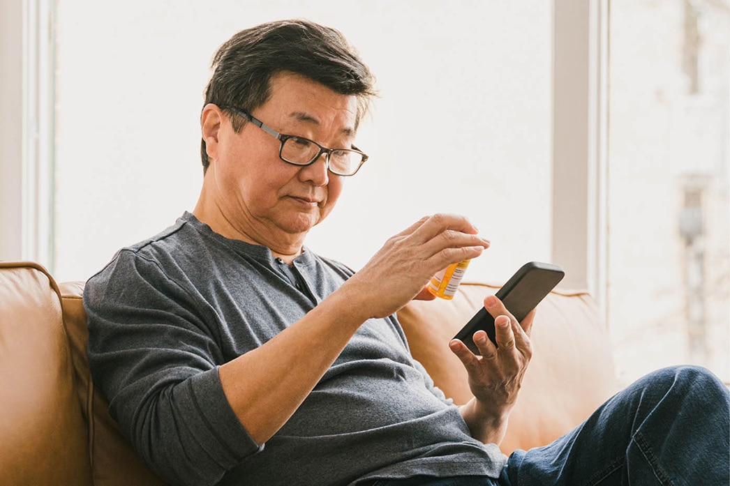 Persona sosteniendo un dispositivo móvil y mirando un frasco de medicamentos