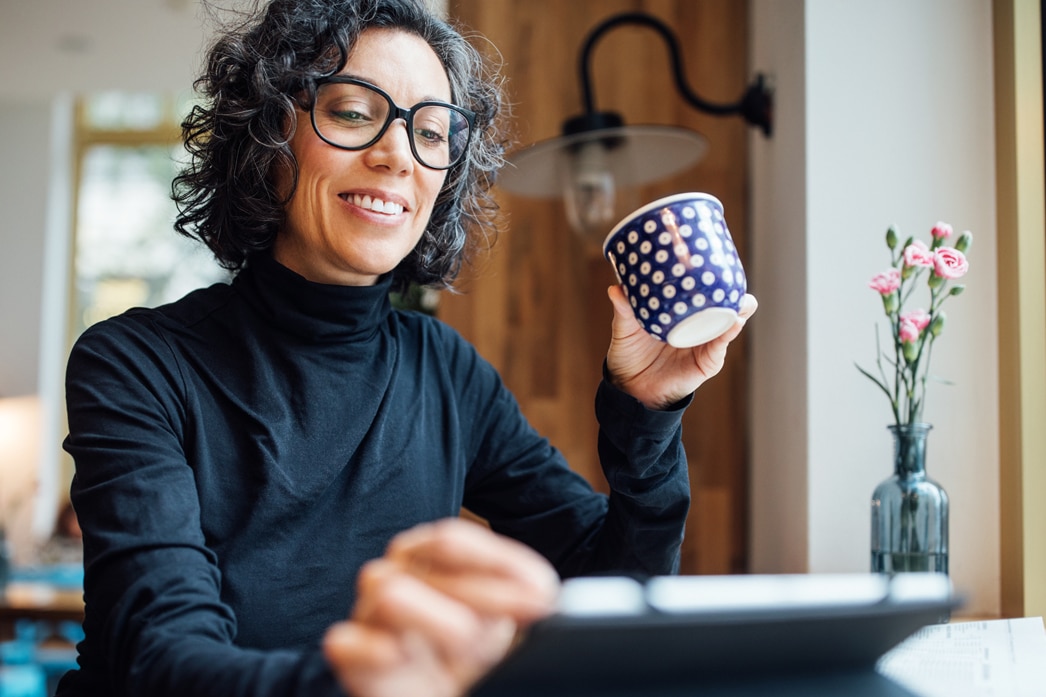 Persona con una taza tomando café mientras lee en una tableta