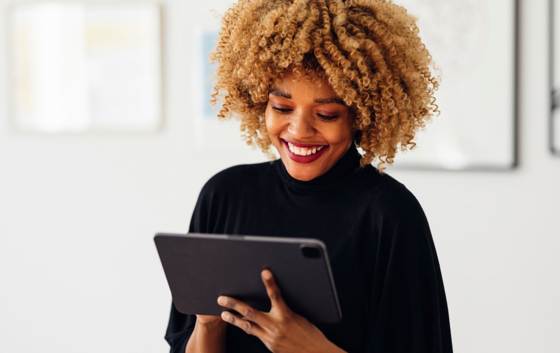 Mujer de negocios feliz sentada en su escritorio usando una tableta