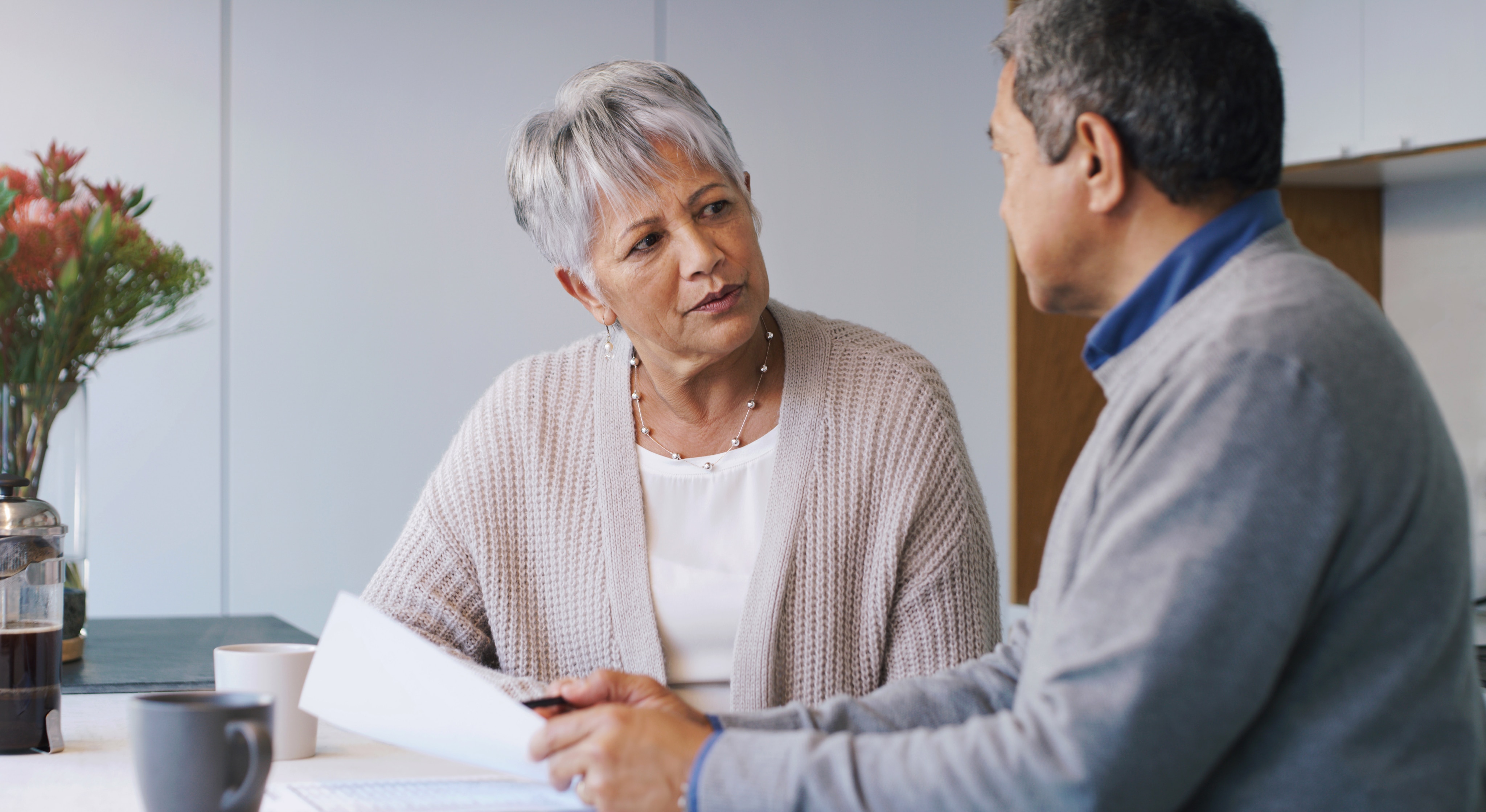 Two people sitting at a table indoors, reviewing papers during a conversation