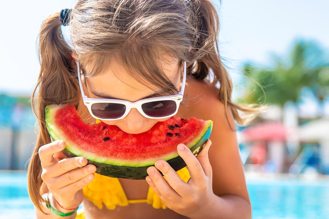 Niña comiendo sandía al lado de una piscina