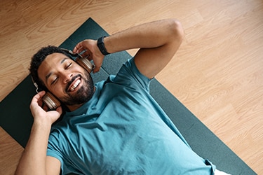 Persona recostada sobre una colchoneta escuchando algo con auriculares