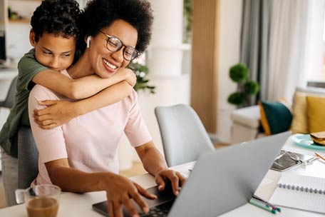 Persona usando una computadora portátil y siendo abrazada por un niño