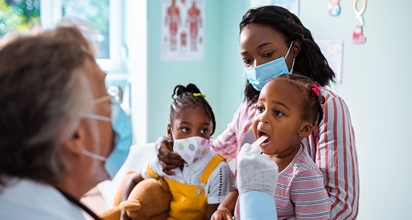 Persona que sostiene a sus hijas mientras el pediatra las examina