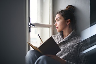 Persona que mira por una ventana sosteniendo un diario