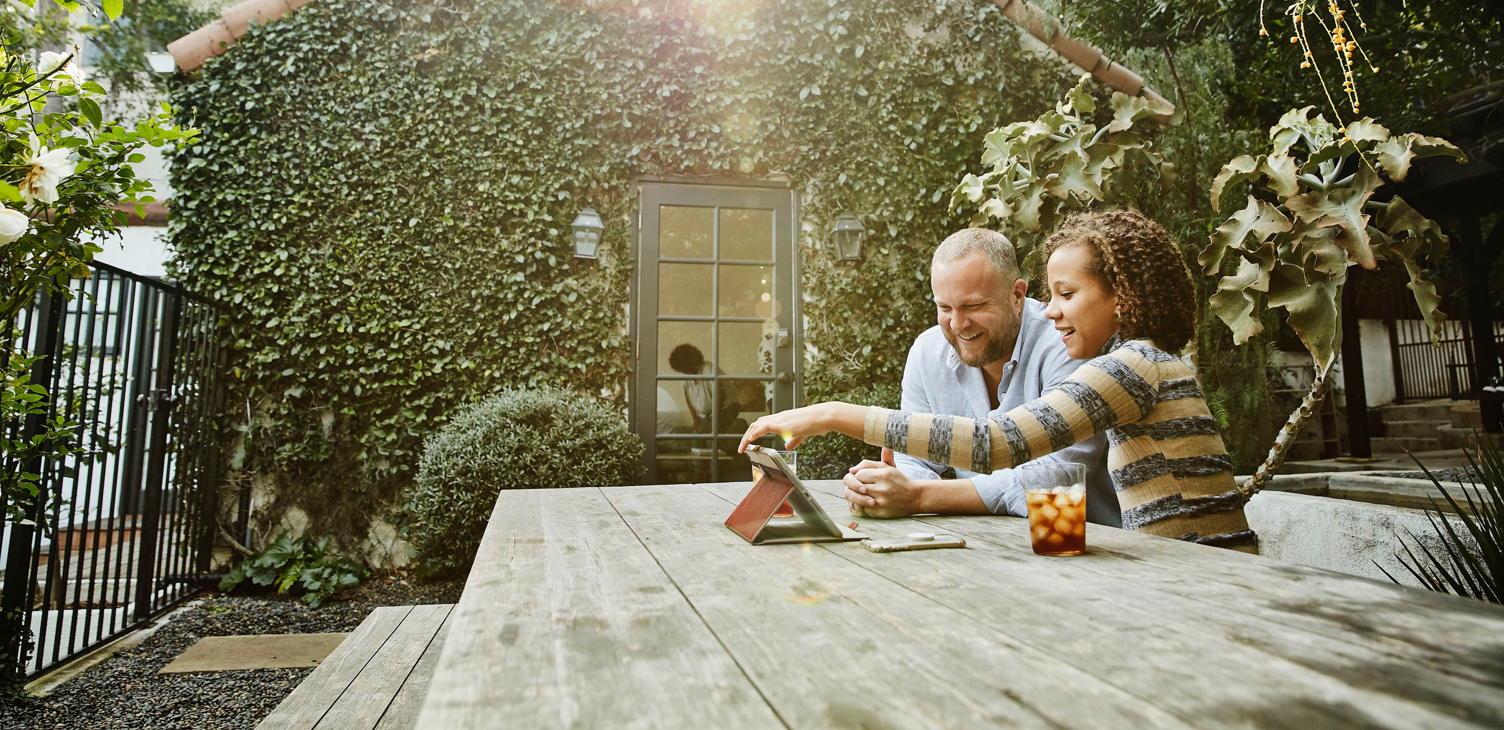 Smiling father and daughter watching video on digital tablet in backyard