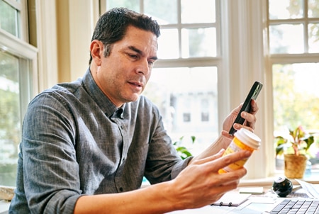 Persona sosteniendo un frasco de medicamentos y un teléfono celular