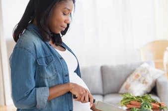 Persona embarazada cortando verduras en la cocina