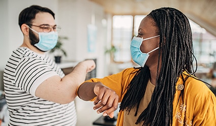 Dos compañeros de trabajo usando mascarilla y chocando codos