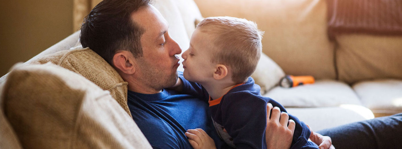 Photo of man and child hugging on couch Photo of man and child hugging on couch