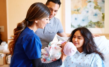nurse handing woman newborn baby