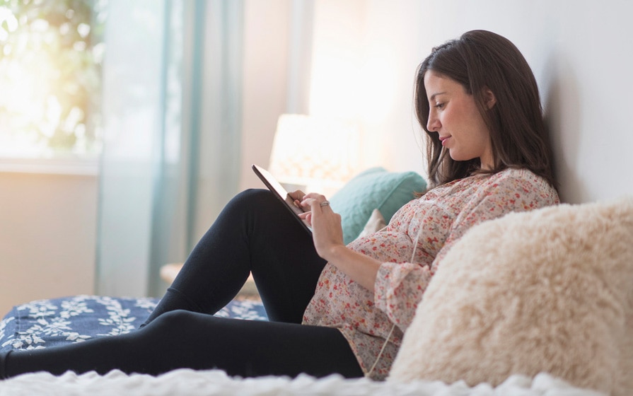 pregnant woman reading tablet in bed