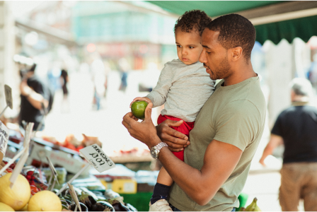 Hombre sosteniendo a un niño en un mercado de productos al aire libre