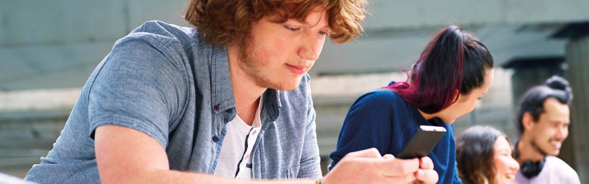 Teenage boy looking at his phone with friends nearby