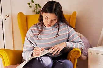 Persona joven sentada y escribiendo un diario