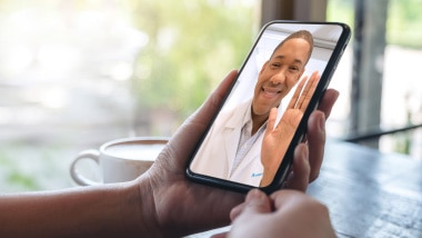 Un médico saluda a un paciente durante una consulta por video en un teléfono inteligente.