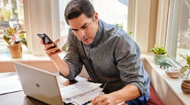 man writes while looking at laptop